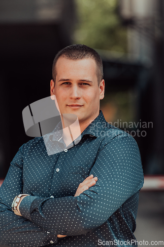 Image of A successful young businessman in a shirt, with crossed arms, poses outdoors, confident expression on his face.