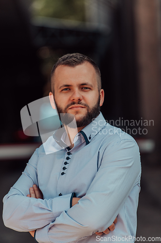 Image of A successful young businessman in a shirt, with crossed arms, poses outdoors, confident expression on his face.