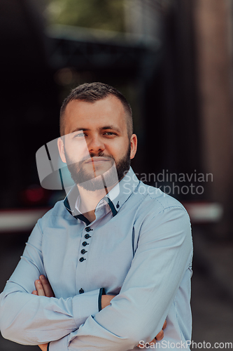 Image of A successful young businessman in a shirt, with crossed arms, poses outdoors, confident expression on his face.