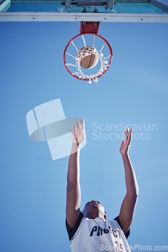 Image of Basketball jump, goal and man on court playing a game low angle for mock up. Motivation, fitness and healthy lifestyle mindset of athlete. Dedicated sports person outside with a blue sky background.