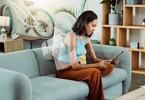 Image of Browsing for movies to watch online on a tablet, streaming videos and scrolling on social media while relaxing on the couch alone at home. Stylish, trendy and casual female browsing the internet