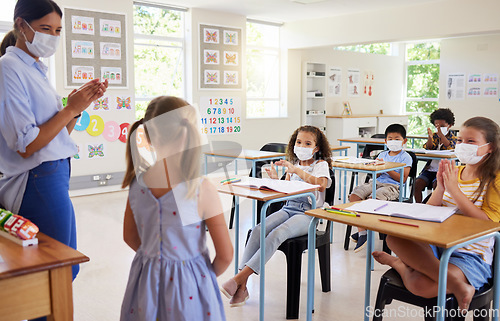 Image of Covid, education and learning with a teacher wearing a mask and clapping for a student after her oral with classmates in class during school. Young girl talking or sharing her answer in a classroom