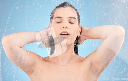 Image of Water, woman and body shower on blue background for healthy skincare, beauty and wellness. Young studio model, water splash and washing hair for personal hygiene, self care and cleaning in bathroom