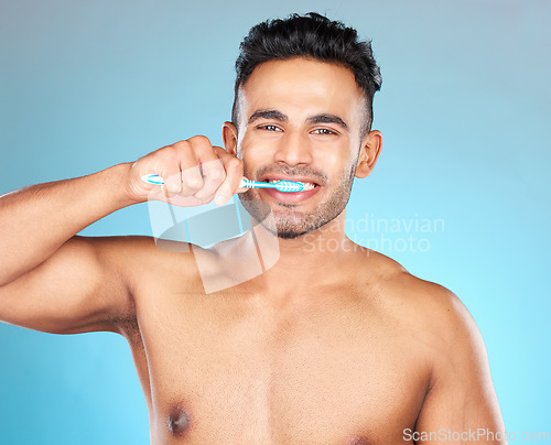 Image of Man, brushing teeth and studio for health, dental care and beauty with smile on face by blue background. Model, portrait and cleaning teeth for hygiene, wellness and healthcare by for healthy mouth