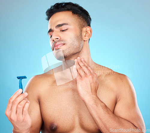 Image of Skincare, shaving and man with razor in studio on blue background for wellness, beauty and self care. Grooming, facial treatment and male face with worry, concern and anxiety to shave sensitive skin