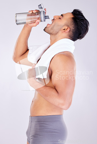 Image of Man drinking water with bottle, underwear and towel after gym workout or fitness training after shower. Health, wellness and hydration, personal trainer standing drinking water with studio background