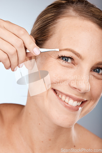 Image of Portrait of woman, tweezers and eyebrow hair removal for clean cosmetics, face and beauty on studio background in Australia. Happy mature model pull hair for brows shape, skincare and facial wellness
