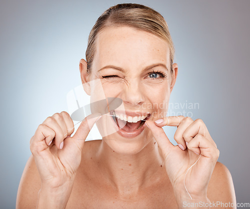 Image of Smile, wink and woman flossing teeth, morning dental care routine on studio background. Health, wellness and happy woman with dental floss, motivation for cleaning a healthy mouth and fresh breath.