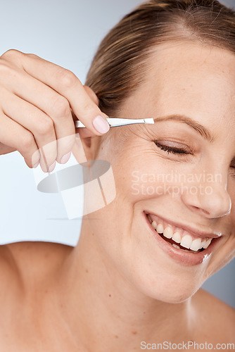 Image of Woman, face and eyebrow hair on face with tweezers and cosmetic therapy in studio grey background. Facial, clean and makeup in beauty, natural cosmetics with tool and clean skincare with happy smile