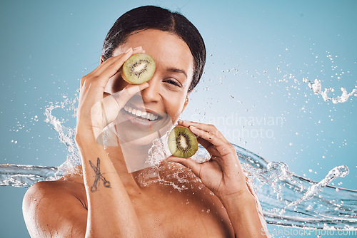 Image of Skincare, water and portrait of woman with kiwi for natural, organic and healthy beauty products in studio. Dermatology, wellness and girl with fruit, water splash and cosmetics on blue background