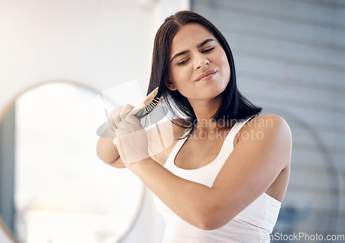 Image of Hair, brush and split ends with a woman in the bathroom of her home, brushing her knots for grooming. Stress, beauty and haircare with a frustrated young female using a hairbrush on a messy hairstyle