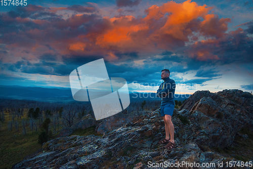 Image of Man standing on top of cliff with fantastic sunset
