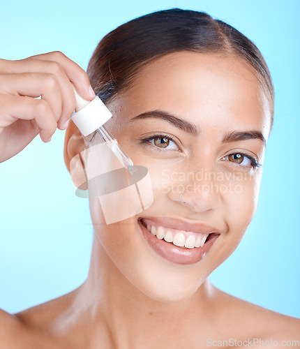 Image of Woman, facial skincare and serum in studio on a blue background to promote a cosmetic product. Face smile, beauty and antiaging with a happy female applying oil to her skin for natural cosmetology