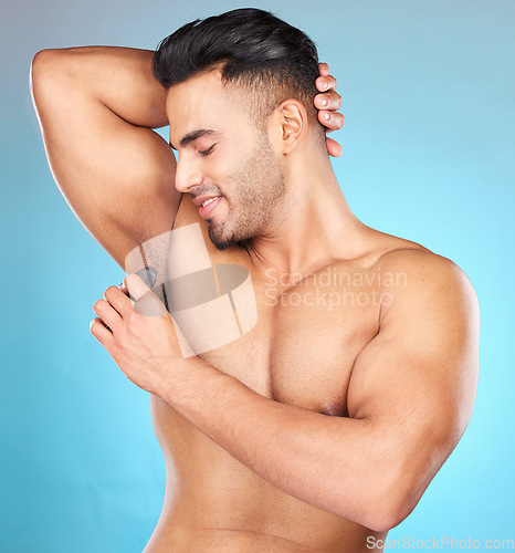 Image of Beauty, body and underarm with a man model applying antiperspirant to his armpit in studio on a blue background. Product, grooming and perfume with a male using roll on to smell fresh or clean