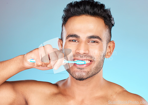 Image of Face portrait, dental and man brushing teeth in studio isolated on a blue background. Wellness, oral health and routine of happy male model holding toothbrush for hygiene, oral care and dental care.
