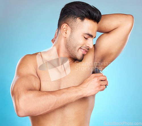 Image of Grooming, armpit and man shaving body hair for hygiene, health and wellness on a blue studio background. Indian model for epilation with electric shaver for hair removal for clean underarm and skin