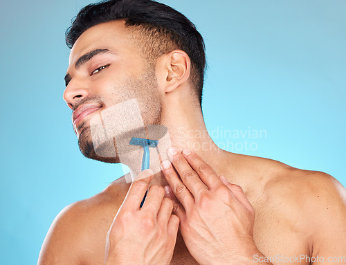 Image of Man shaving, razor and grooming beard or facial hair for self care, skincare and body wellness on blue studio background. Face of indian model with a smile for clean shave, cosmetics and healthy skin