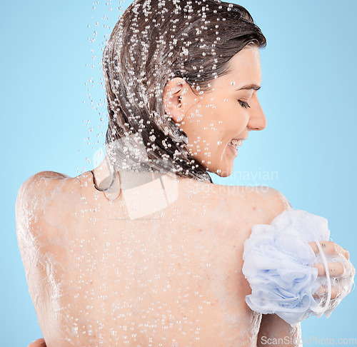 Image of Back, shower and woman with loofah, wellness and water for natural beauty, health and against blue studio background. Young female, healthy lady and washing for skincare, liquid drops and relax.