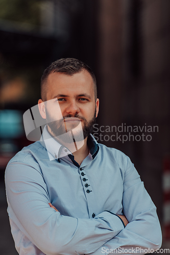 Image of A successful young businessman in a shirt, with crossed arms, poses outdoors, confident expression on his face.