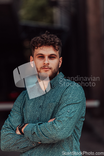 Image of A successful young businessman in a shirt, with crossed arms, poses outdoors, confident expression on his face.