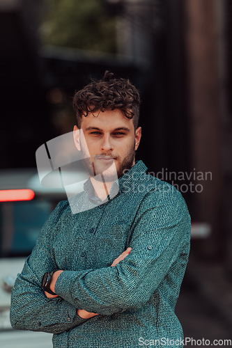 Image of A successful young businessman in a shirt, with crossed arms, poses outdoors, confident expression on his face.