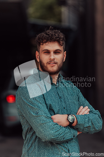 Image of A successful young businessman in a shirt, with crossed arms, poses outdoors, confident expression on his face.