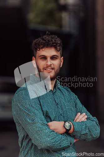 Image of A successful young businessman in a shirt, with crossed arms, poses outdoors, confident expression on his face.