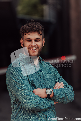 Image of A successful young businessman in a shirt, with crossed arms, poses outdoors, confident expression on his face.