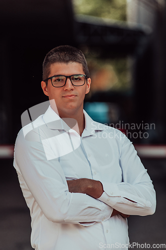 Image of A successful businessman in a white shirt, with crossed arms, poses outdoors, confident expression on his face.