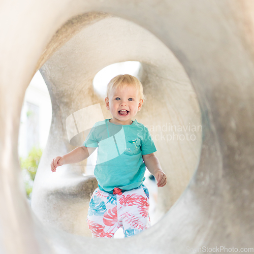 Image of Child playing on outdoor playground. Toddler plays on school or kindergarten yard. Active kid on stone sculpured slide. Healthy summer activity for children. Little boy climbing outdoors.