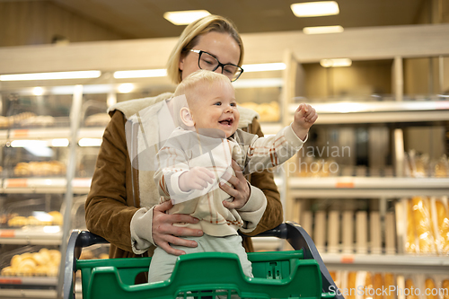 Image of Caucasian mother shopping with her infant baby boy child choosing products in department of supermarket grocery store.