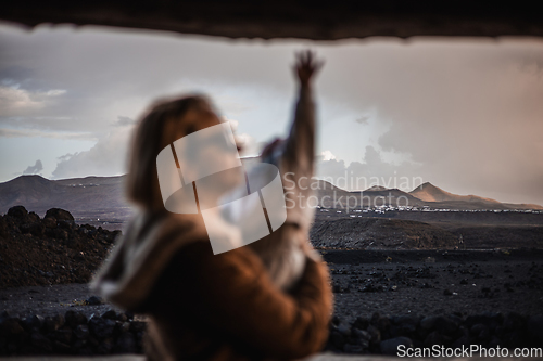 Image of Mother enjoying winter vacations playing with his infant baby boy son on black sandy volcanic beach of Janubio on Lanzarote island, Spain on windy overcast day. Family travel vacations concept.