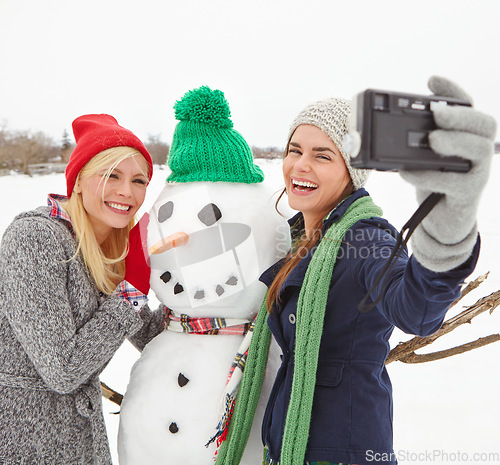 Image of Selfie, snowman and winter with woman friends taking a photograph outdoor together in the snow. Happy, smile and photography with a young female and friend posing for a picture in the cold weather