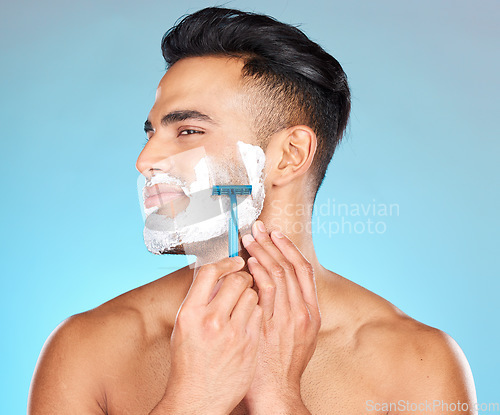 Image of Studio, skincare and man shaving beard with razor blade for beauty wellness, grooming or self care on blue background. Hair removal, face or model cutting facial hair in morning routine with product