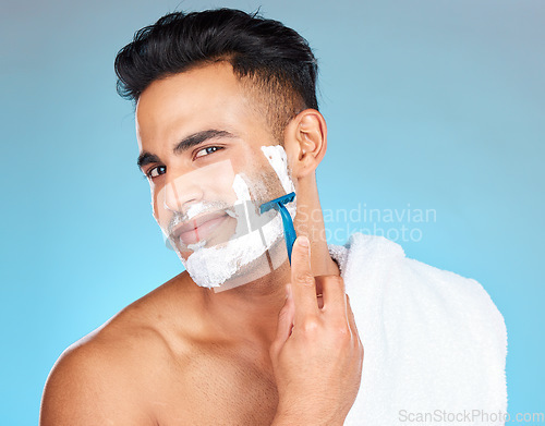 Image of Man, face and shaving in studio for skincare, wellness and towel in portrait by blue background. Model, facial hair removal and cosmetic cream for skin, self care and cleaning with cosmetics beauty