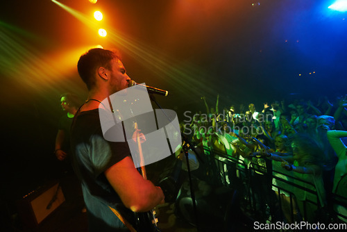 Image of Concert, band and music with a man guitarist playing at a gig for a crowd or audience at a performance event. Festival, stage and social with a male artist strumming a guitar while singing at a show