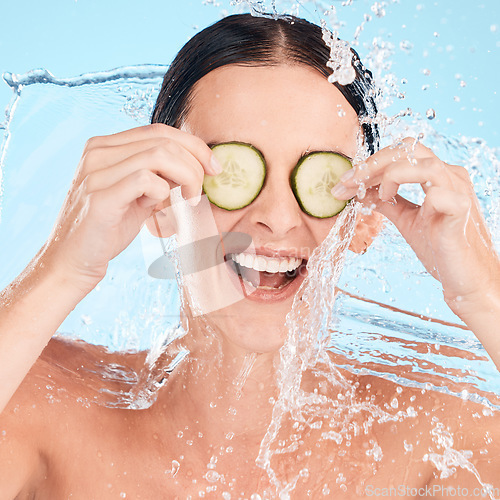 Image of Water, beauty and cucumber with a woman in the shower in studio on a blue background for hygiene or hydration. Health, wellness and luxury with an attractive young female in the bathroom for skincare