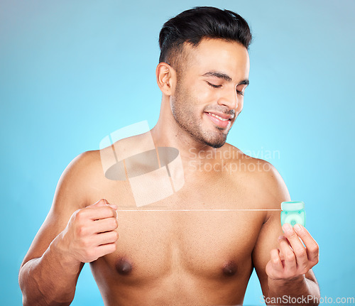 Image of Man, body or dental floss for grooming, mouth hygiene maintenance or plaque removal help on blue background in studio. Smile, happy or flossing model and teeth product in healthcare wellness cleaning