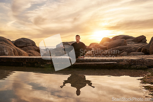 Image of Sunset, yoga or zen man in meditation by a calm or peaceful lake or beach for a spiritual mindfulness exercise. Nature, wellness or healthy yogi in a lotus pose training his relaxed body to meditate