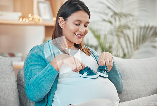 Image of Pregnant woman, sofa and relax with baby shoes in hands for child with a happy smile, love and excitement. Pregnancy, cute trainers and a new mom on maternity leave on couch in apartment living room
