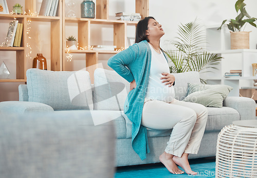 Image of Pregnant, woman and back pain with a mother feeling painful body while sitting on her couch. Ache, inflammation and pregnancy with a maternity female with physical strain in her back at home