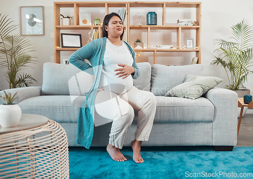 Image of Pregnant woman, discomfort and back pain sitting on the living room sofa and holding tummy at home. Female going through pregnancy contractions, pain or medical health issues and back ache on couch