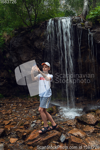 Image of Boy tourist taking selfie photos with a smartphone at the waterfalls