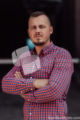 Image of A successful young businessman in a shirt, with crossed arms, poses outdoors, confident expression on his face.