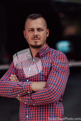 Image of A successful young businessman in a shirt, with crossed arms, poses outdoors, confident expression on his face.