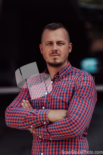 Image of A successful young businessman in a shirt, with crossed arms, poses outdoors, confident expression on his face.