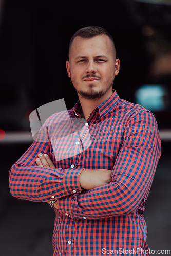 Image of A successful young businessman in a shirt, with crossed arms, poses outdoors, confident expression on his face.