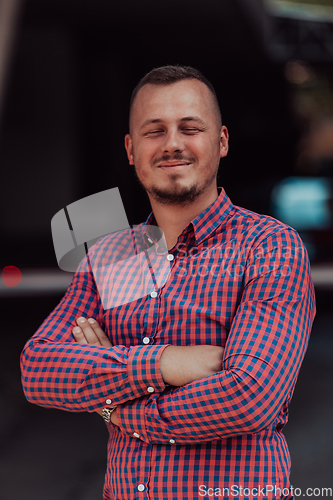 Image of A successful young businessman in a shirt, with crossed arms, poses outdoors, confident expression on his face.