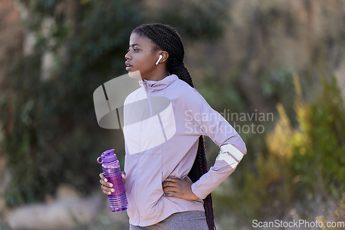 Image of Fitness, running and black woman with water bottle in nature for wellness, minerals and healthy lifestyle. Exercise, sports and girl with earphones rest, breathe and relax after marathon training