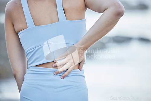 Image of Woman runner, back pain and hand for massage, physical therapy or self care at outdoor training. Girl, lower back injury and nature workout for health, fitness and wellness in summer morning at beach
